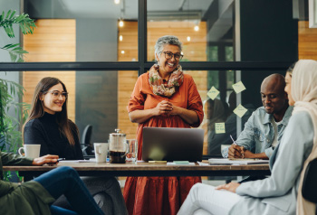 Five diverse individuals sitting around a table in a meeting room, engaged in conversation.