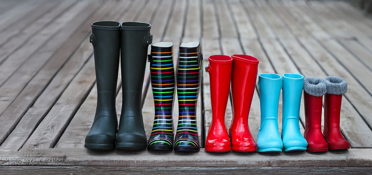 A row of rubber boots of decreasing sizes on a rustic porch.