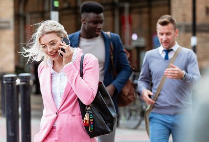 A business woman in a pink suit talking on the phone while crossing the street.