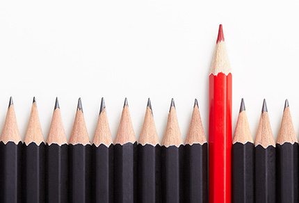 A line of black pencil crayons with one red pencil crayon standing taller.