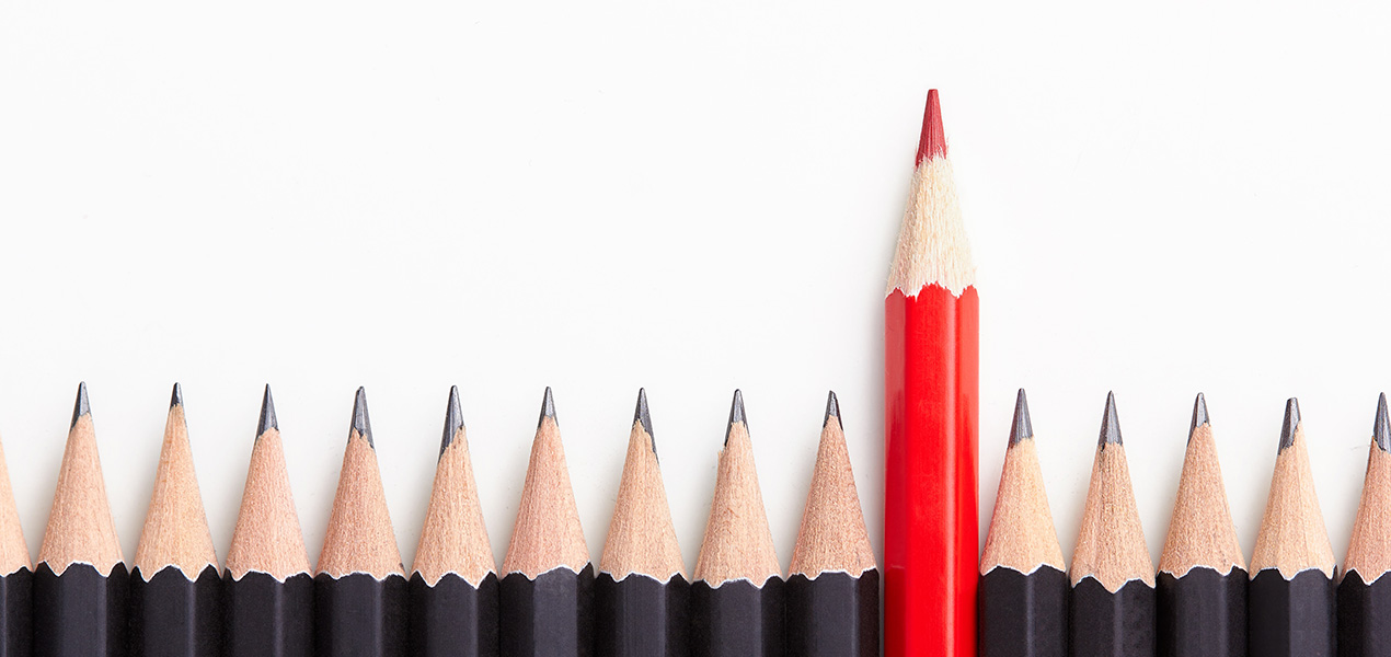 A line of black pencil crayons with one red pencil crayon standing taller.