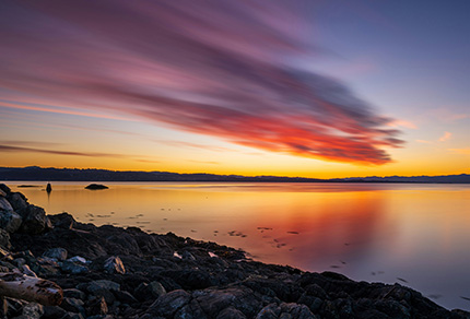 A body of water with a rocky shore at sunset