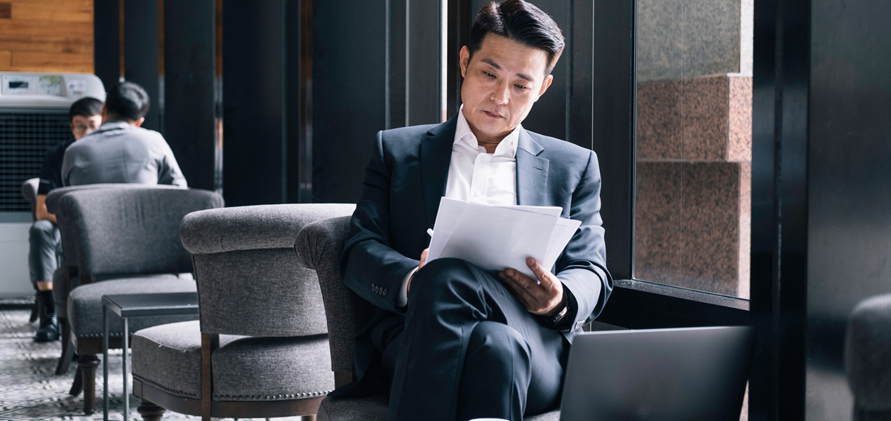 Asian business man sitting in a chair looking at some papers.