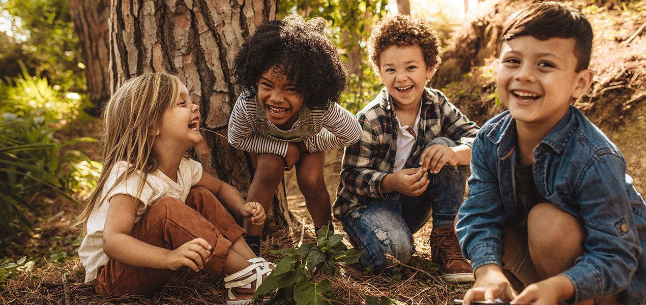 Group of smiling diverse kids sitting together in forest and looking at camera.
