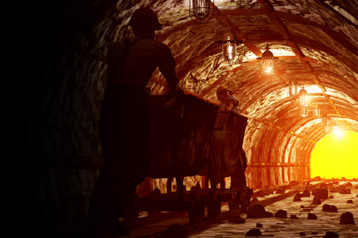 A miner pushing a trolley down a dark tunnel.