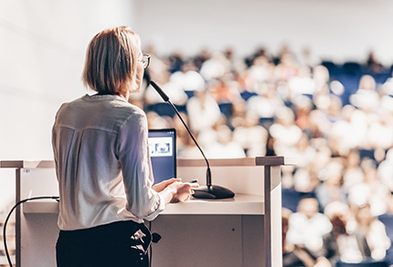 A woman standing at a podium speaking to a large audience.