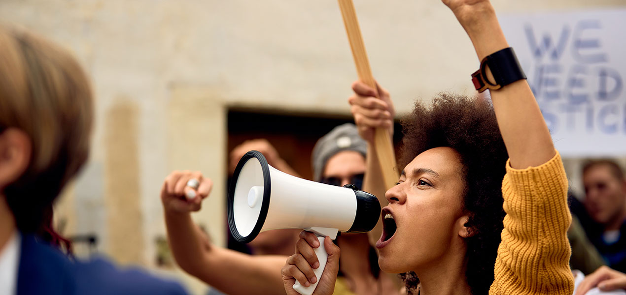 A young woman raises her fist while shouting through megaphone at a protest.