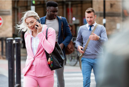 A business woman in a pink suit talking on the phone while crossing the street.