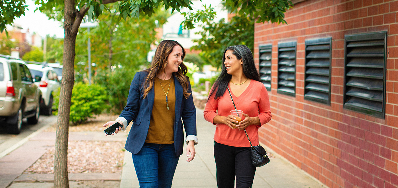 Two professional women walking and talking down a quiet city street.