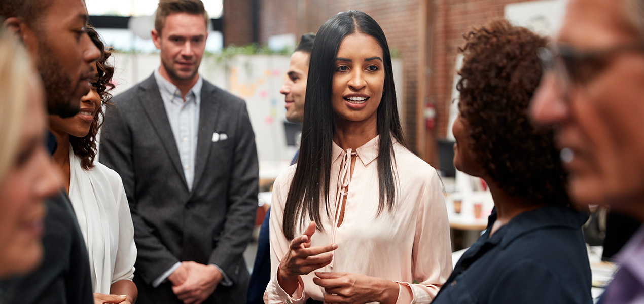 A young business woman networking at an event with multiple people.