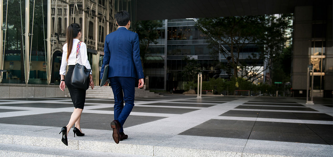 Two young professional walking up the stairs to an office building in a city. 