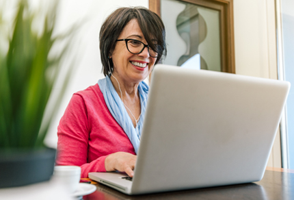 Mature woman wearing a headset, working on laptop.