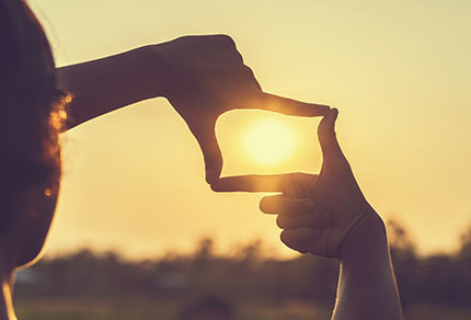 A person framing the sun with their thumb and forefinger.