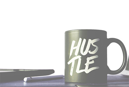 A mug with the word "Hustle" on it sitting on an office desk.