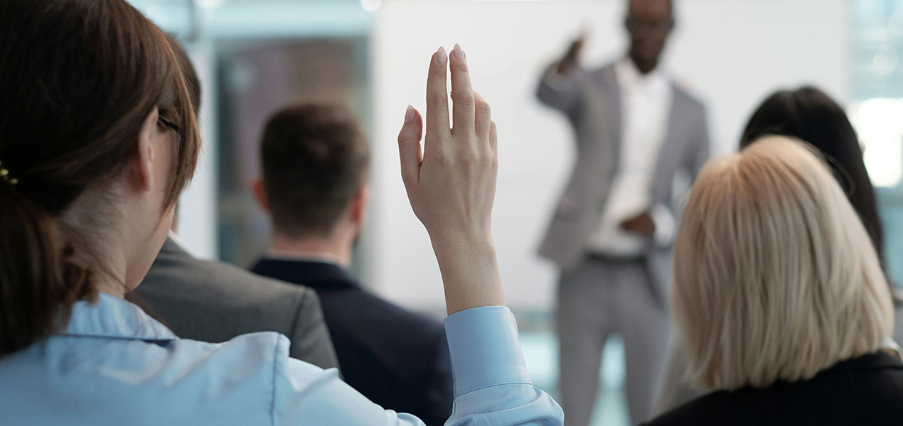 In a large audience, a female participant raises her hand.