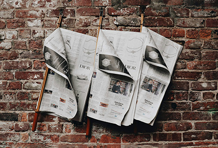 Three newspapers hung up against a brick wall.