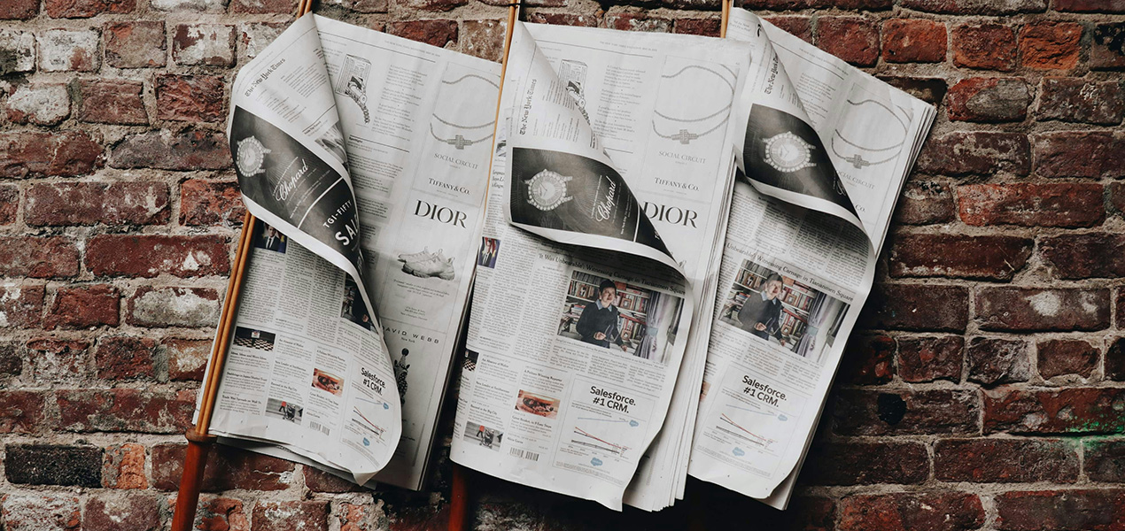 Three newspapers hung up against a brick wall.