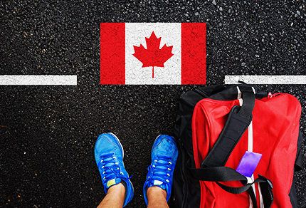An aerial view of a person standing on a street with a Canadian flag and a duffle bag at their feet.