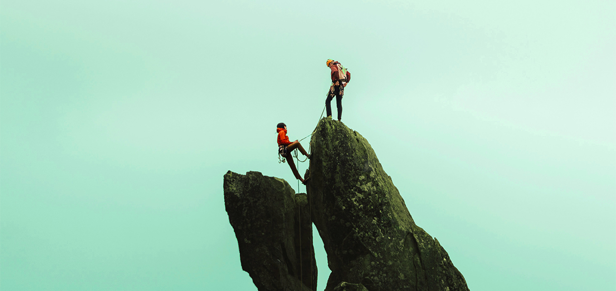 Two rock climbers reaching the summit of a mountain.