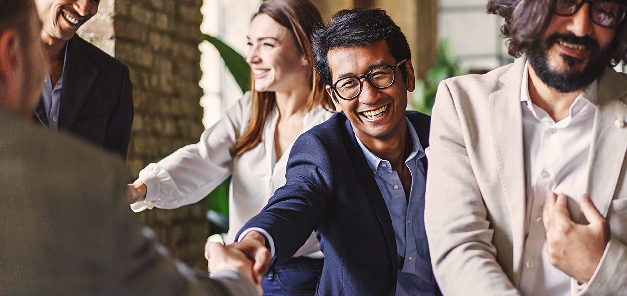 A young professional shaking hands with another person in the middle of a networking event.