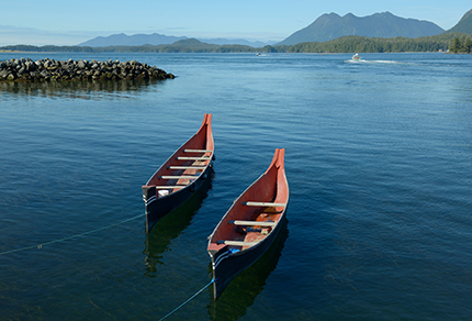 Two Indigenous canoes resting on the shore of the Pacific Ocean.