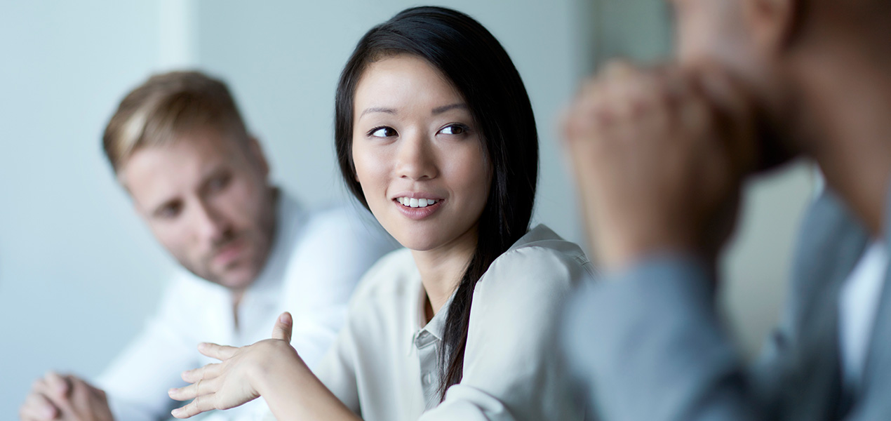Two men listening to a woman speaking during a meeting.