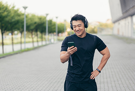 An Asian male on a morning run in the park listens to music and podcast on his phone.