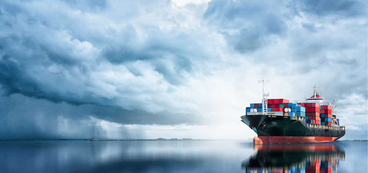 An international container cargo ship in the ocean against a cloudy background.