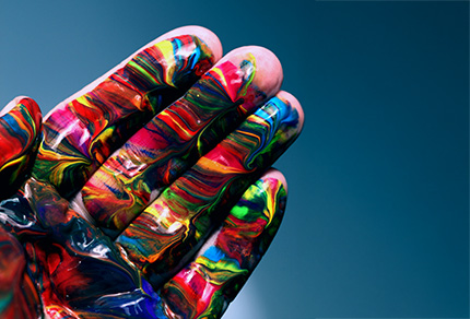 Close up of a hand covered is many different colours of oil paint.