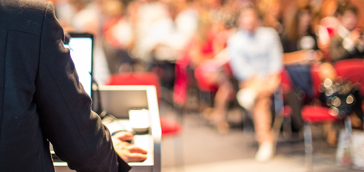 A presenter speaking at a podium in front of a large audience.