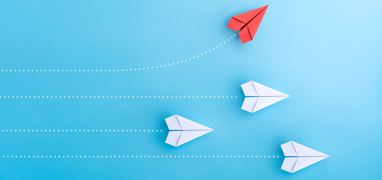 Multiple paper airplanes flying to the right while one breaks off and flies higher.