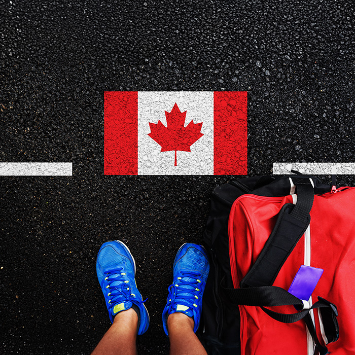 An aerial view of a person standing on pavement with a Canadian flag at their feet.