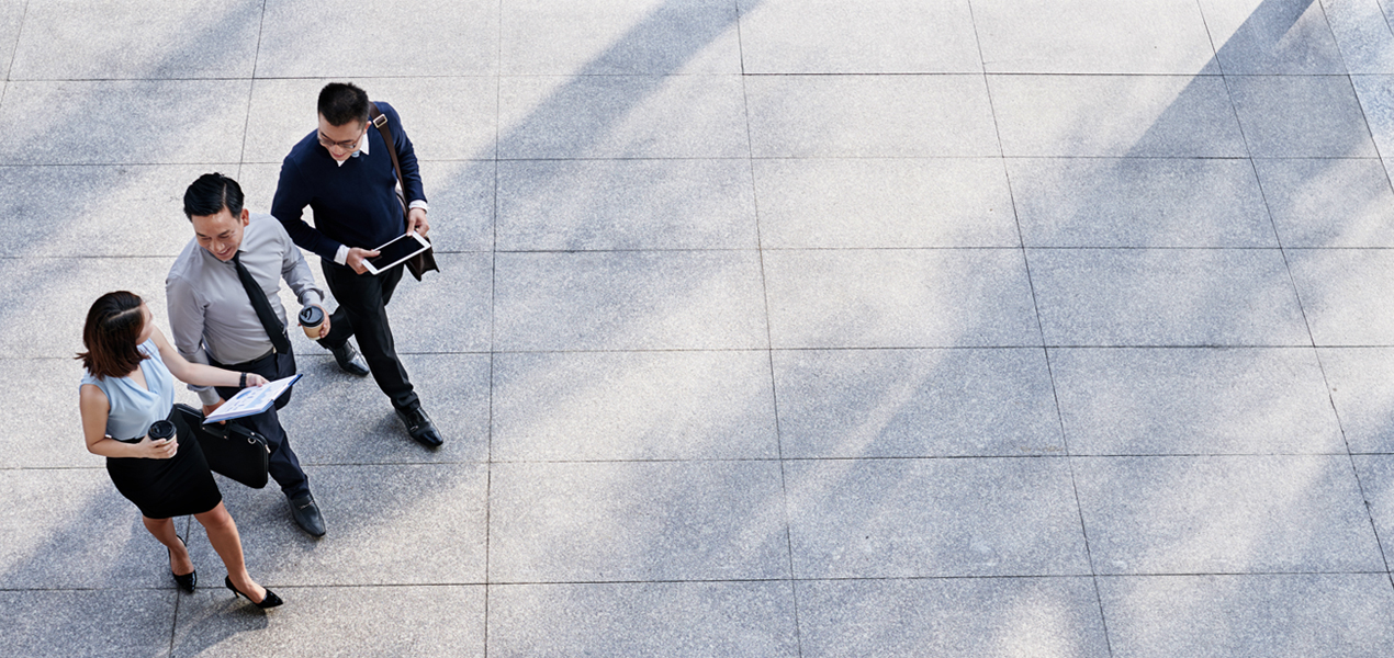 Aerial view of three people in business attire walking outdoors on stone pavement.