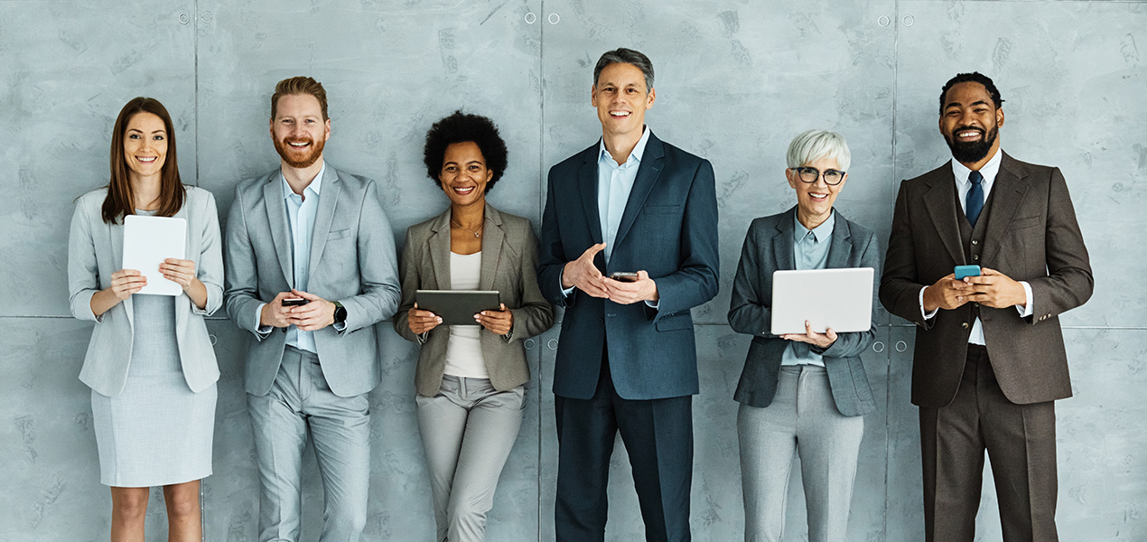A diverse group of professionals standing against a wall looking directly at the camera